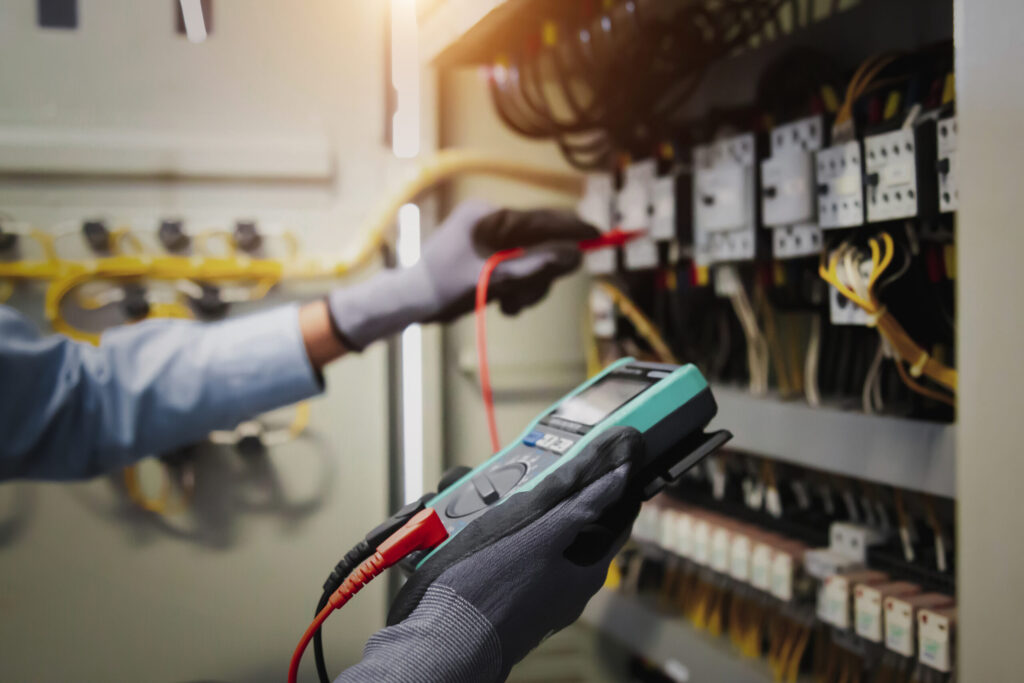 electricity and electrical maintenance service, engineer hand holding ac multimeter checking electric current voltage at circuit breaker terminal and cable wiring main power distribution board.
